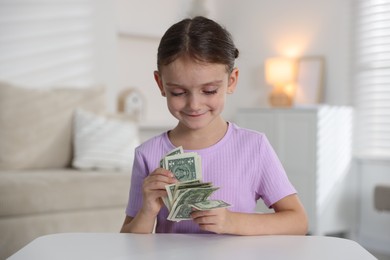 Photo of Little girl holding pocket money at white table indoors