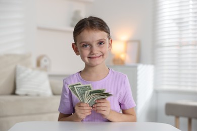 Photo of Little girl holding pocket money at white table indoors