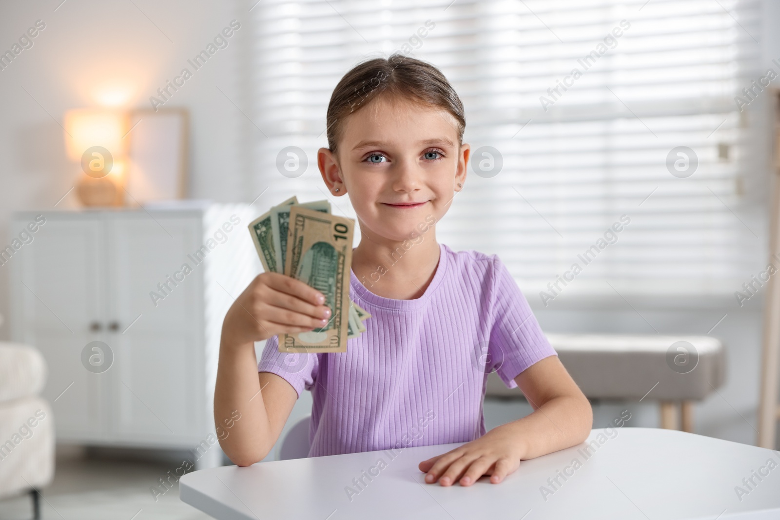 Photo of Little girl holding pocket money at white table indoors