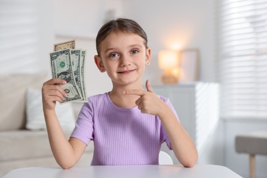 Photo of Little girl holding pocket money at white table indoors