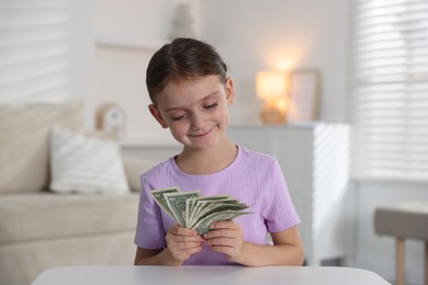 Photo of Little girl holding pocket money at white table indoors
