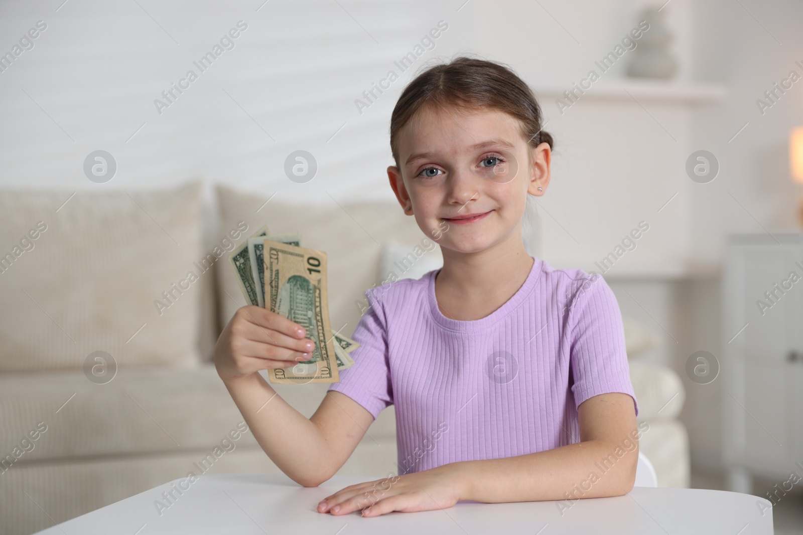 Photo of Little girl holding pocket money at white table indoors