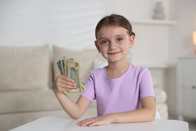 Photo of Little girl holding pocket money at white table indoors