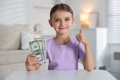 Photo of Little girl holding pocket money at white table indoors