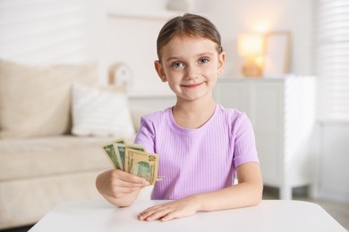 Photo of Little girl holding pocket money at white table indoors