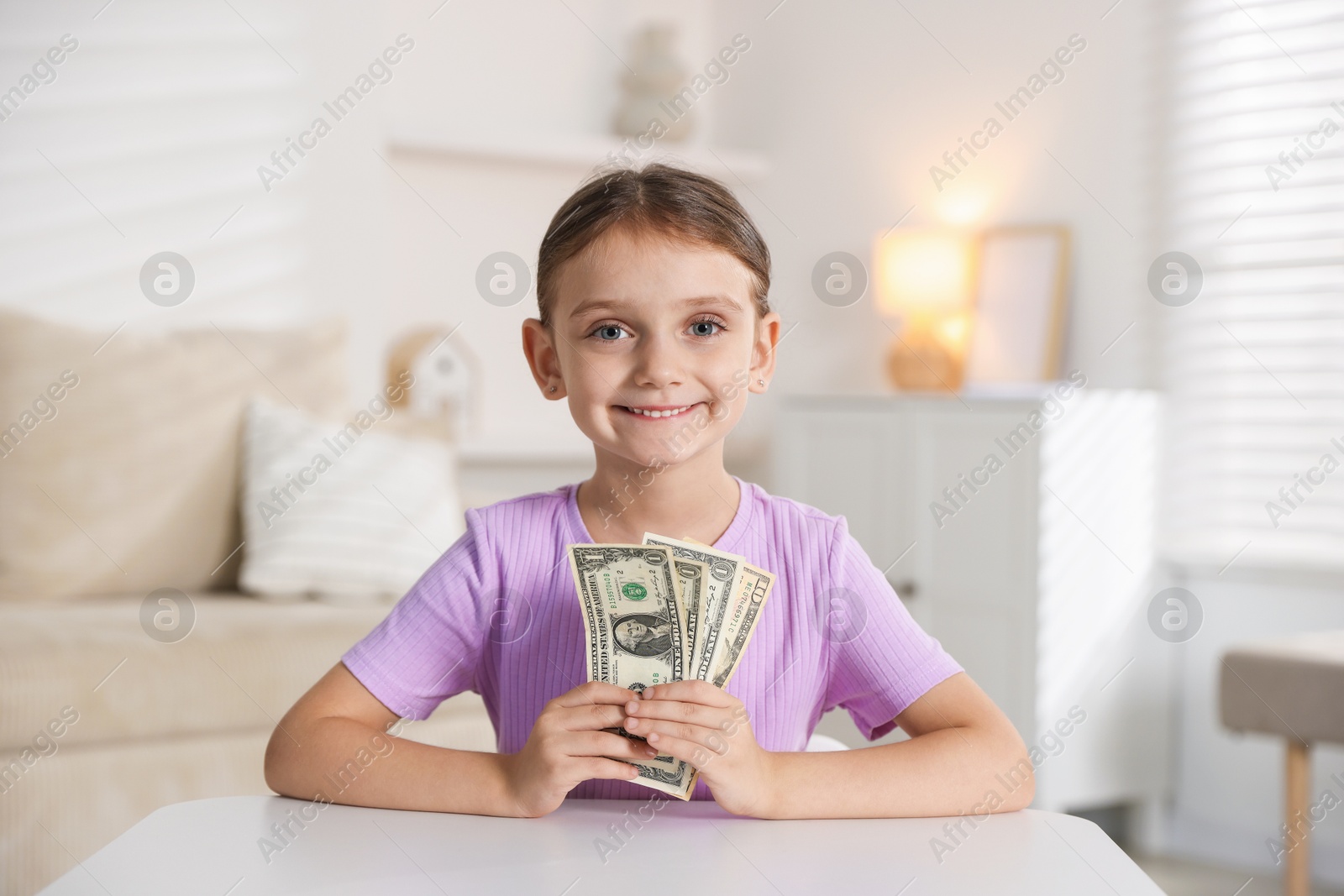 Photo of Little girl holding pocket money at white table indoors