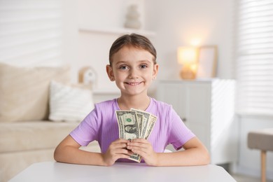 Photo of Little girl holding pocket money at white table indoors