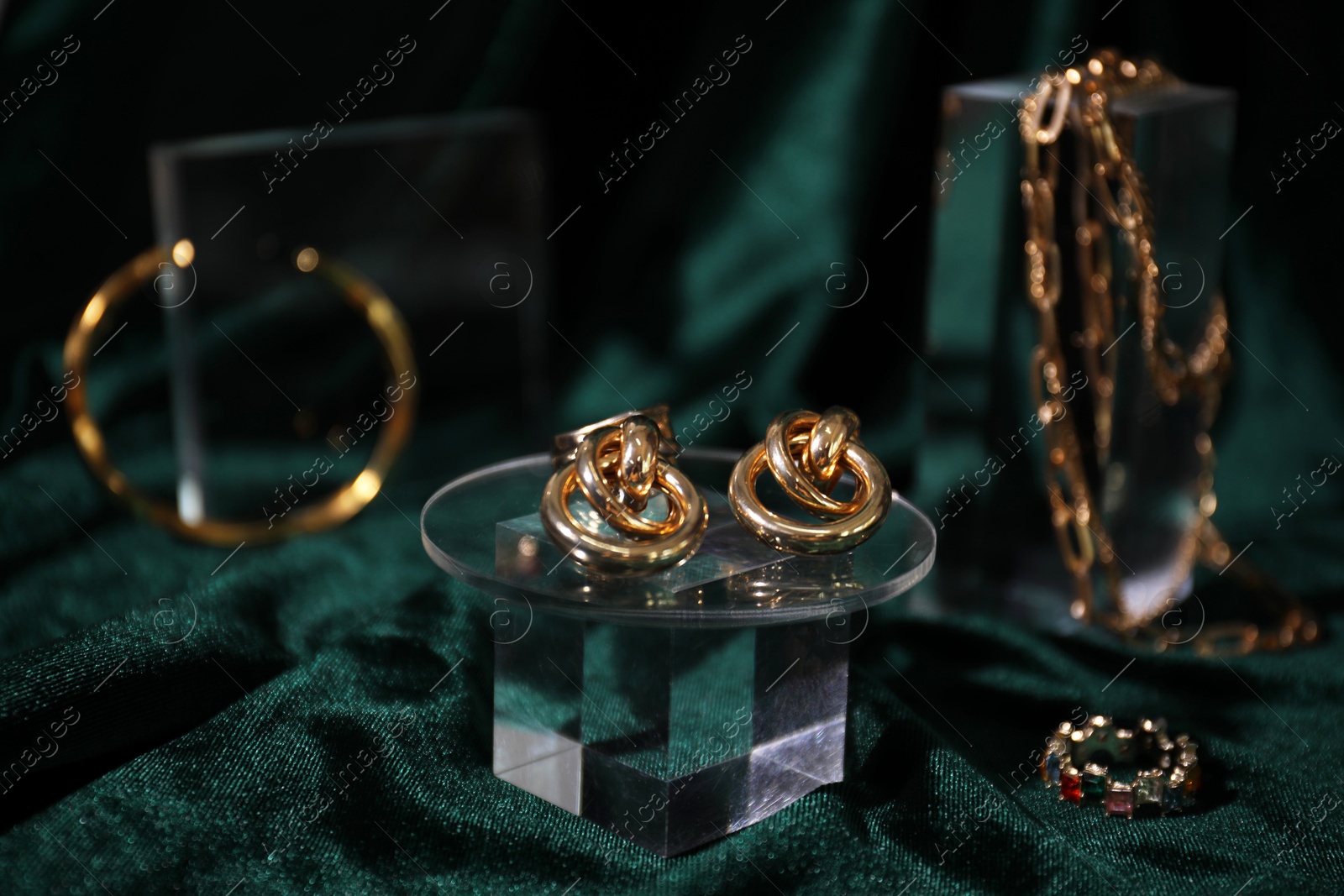 Photo of Stylish presentation of gold earrings and other jewelry on green silk cloth, closeup