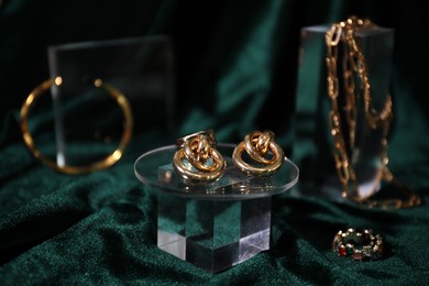 Photo of Stylish presentation of gold earrings and other jewelry on green silk cloth, closeup