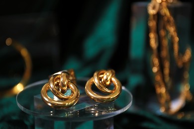 Photo of Stylish presentation of gold earrings on podium against blurred green background, closeup. Space for text