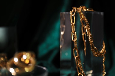 Photo of Stylish presentation of gold necklace on podium against blurred green background, closeup. Space for text