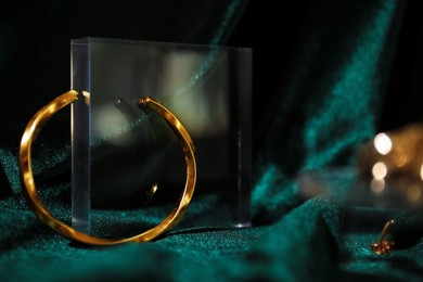 Photo of Stylish presentation of gold bracelet on green silk cloth, closeup. Space for text