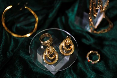 Photo of Stylish presentation of gold jewelry on green silk cloth, above view