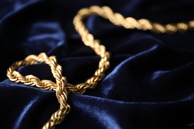 Photo of Stylish gold necklace on blue silk cloth, closeup