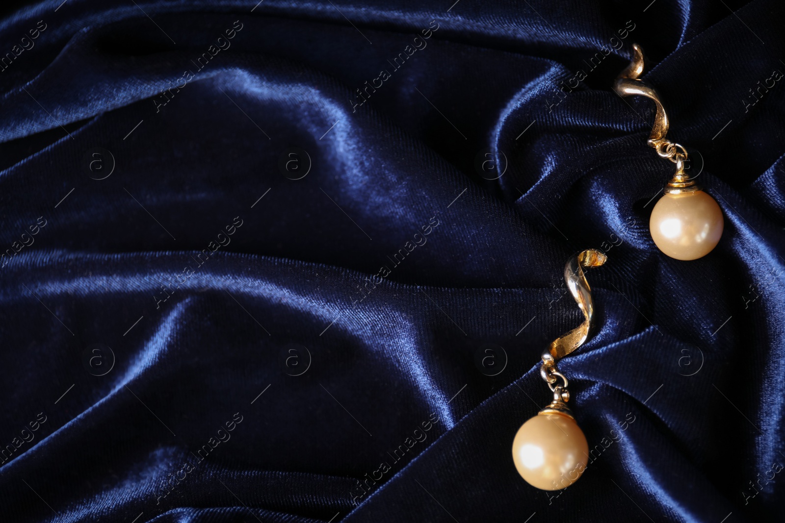 Photo of Stylish gold earrings on blue silk cloth, top view. Space for text