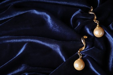 Photo of Stylish gold earrings on blue silk cloth, top view. Space for text