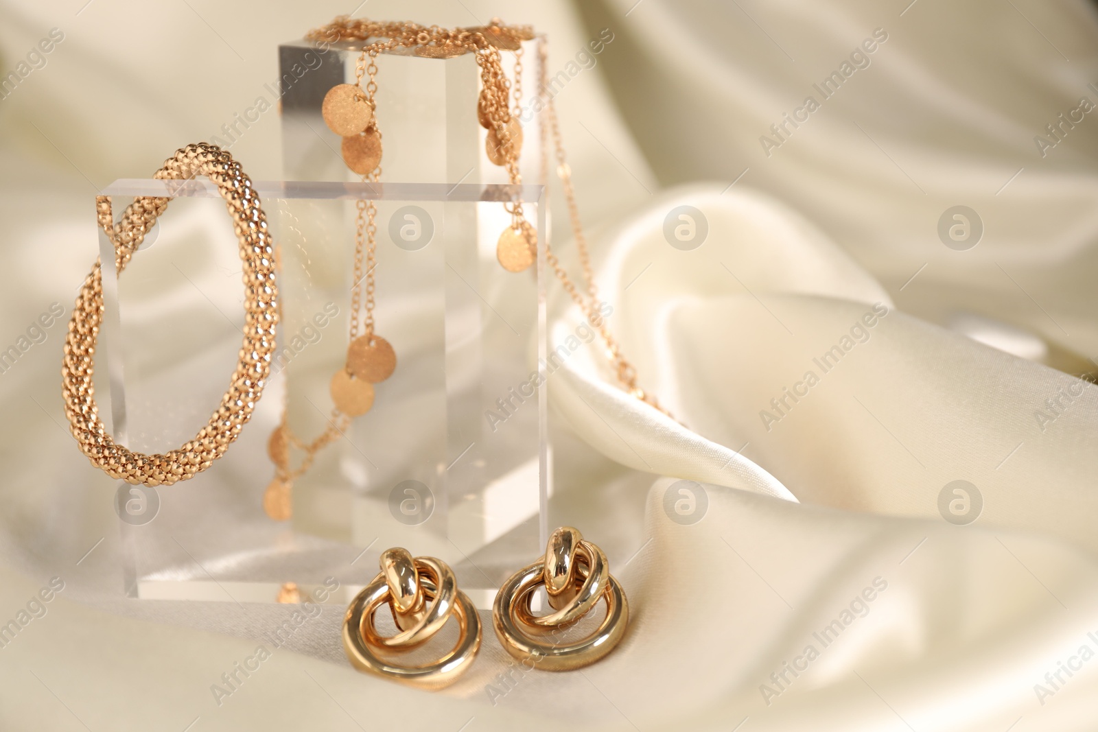 Photo of Stylish presentation of gold jewelry on light silk cloth, closeup. Space for text