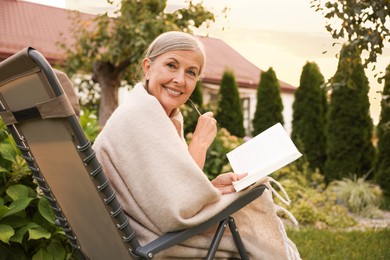 Photo of Senior woman with book and glasses in armchair outdoors