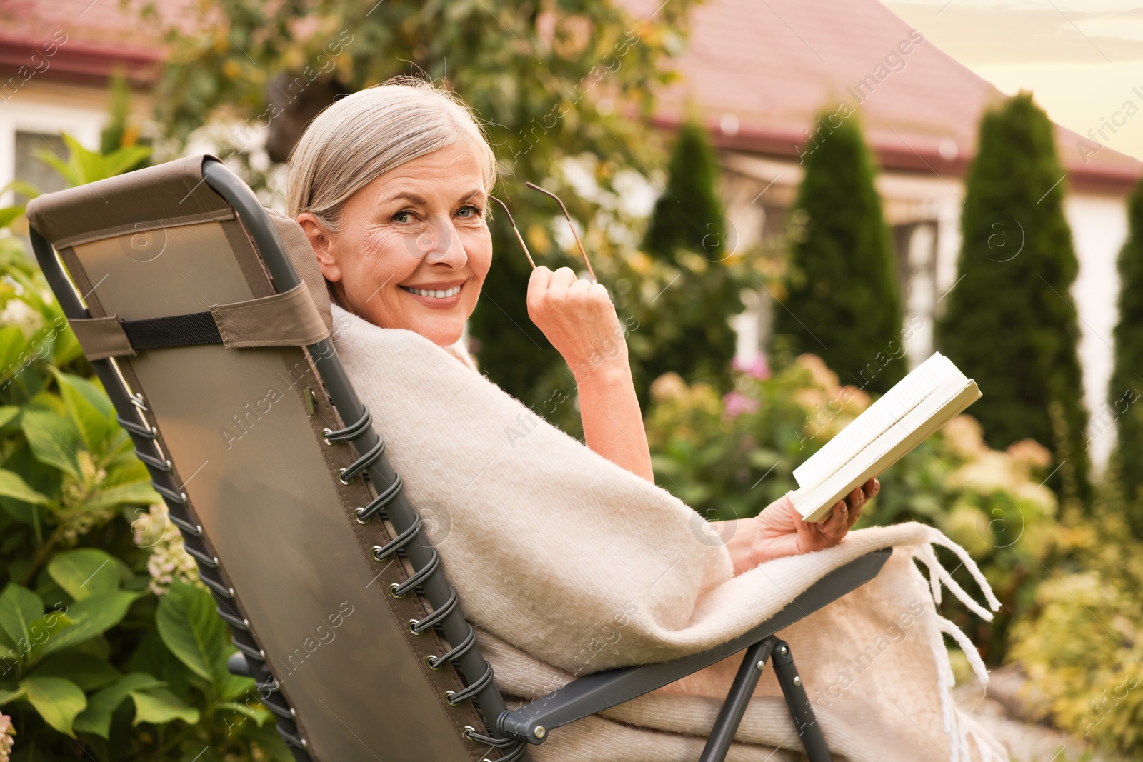 Photo of Senior woman with book and glasses in armchair outdoors