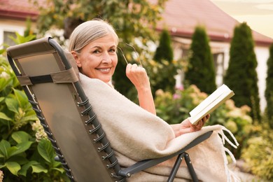Photo of Senior woman with book and glasses in armchair outdoors