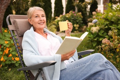 Photo of Senior woman with cup of drink reading book in armchair outdoors