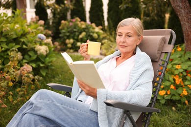 Photo of Senior woman with cup of drink reading book in armchair outdoors