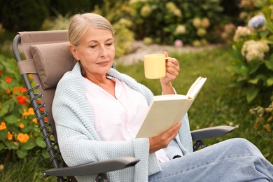 Photo of Senior woman with cup of drink reading book in armchair outdoors