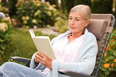 Photo of Senior woman reading book in armchair outdoors