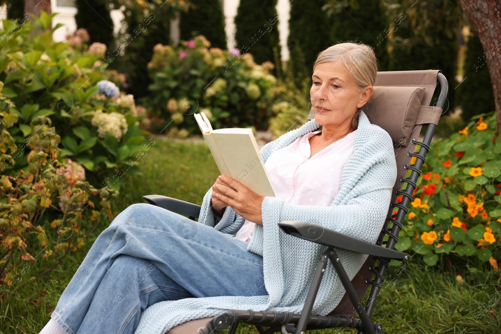 Senior woman reading book in armchair outdoors Photo of Senior woman reading book in armchair outdoors