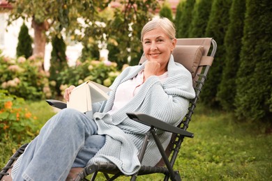 Photo of Senior woman reading book in armchair outdoors