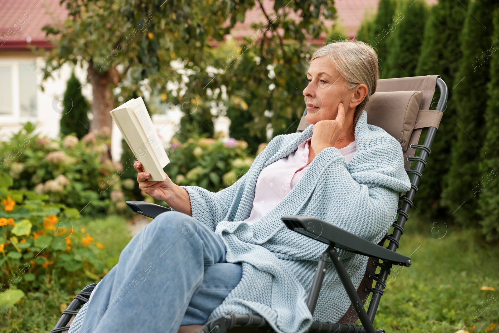 Photo of Senior woman reading book in armchair outdoors