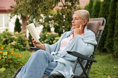 Photo of Senior woman reading book in armchair outdoors