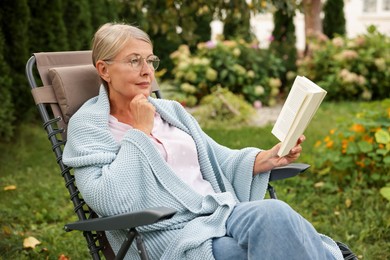 Photo of Senior woman reading book in armchair outdoors