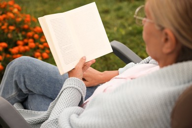 Photo of Senior woman reading book in armchair outdoors, closeup