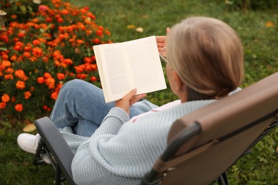 Photo of Senior woman reading book in armchair outdoors