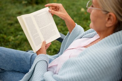 Photo of Senior woman reading book in armchair outdoors, closeup