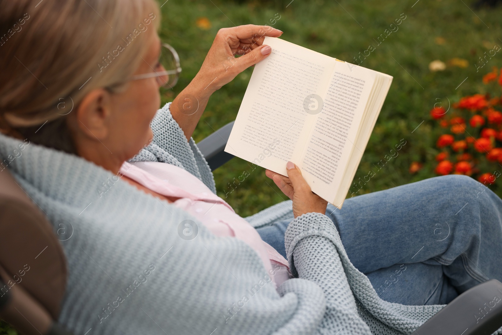 Photo of Senior woman reading book in armchair outdoors
