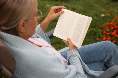 Photo of Senior woman reading book in armchair outdoors