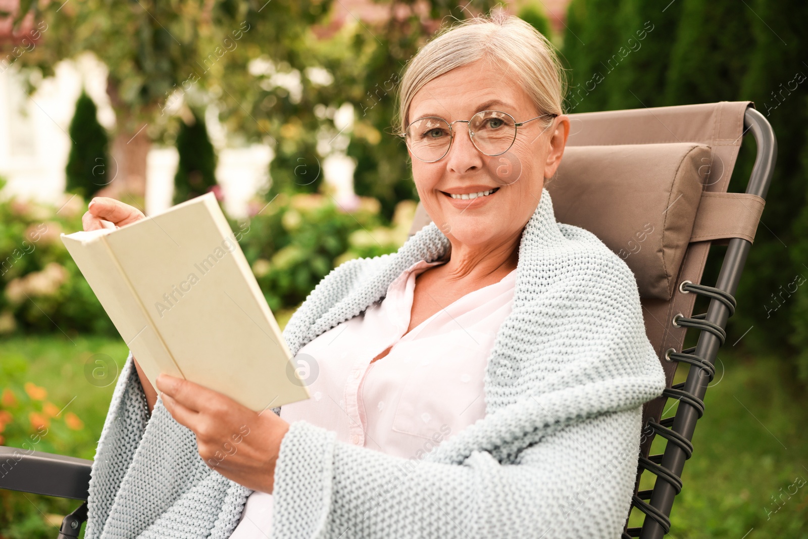 Photo of Senior woman reading book in armchair outdoors