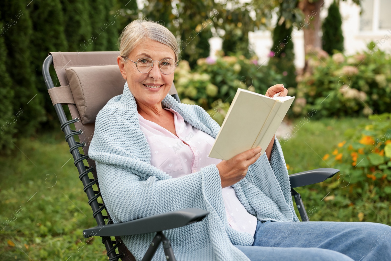 Photo of Senior woman reading book in armchair outdoors