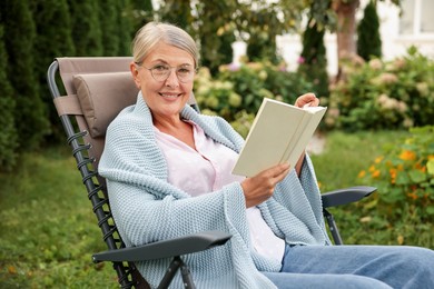 Photo of Senior woman reading book in armchair outdoors