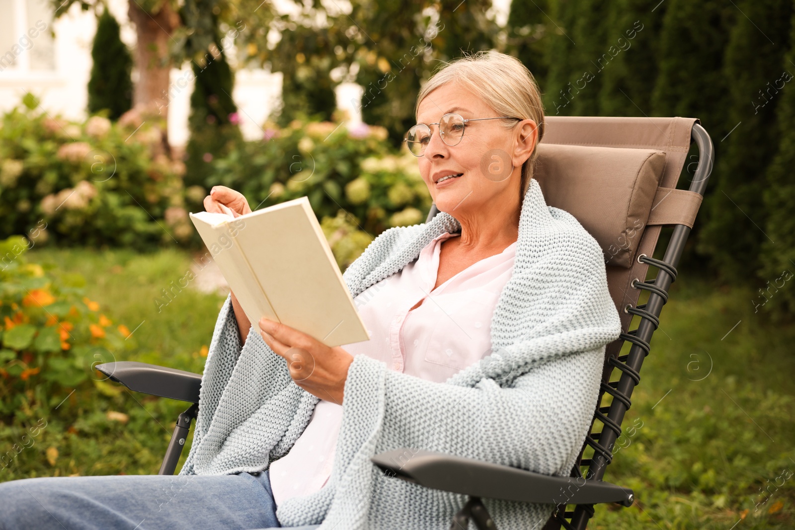 Photo of Senior woman reading book in armchair outdoors