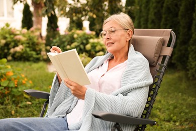 Photo of Senior woman reading book in armchair outdoors