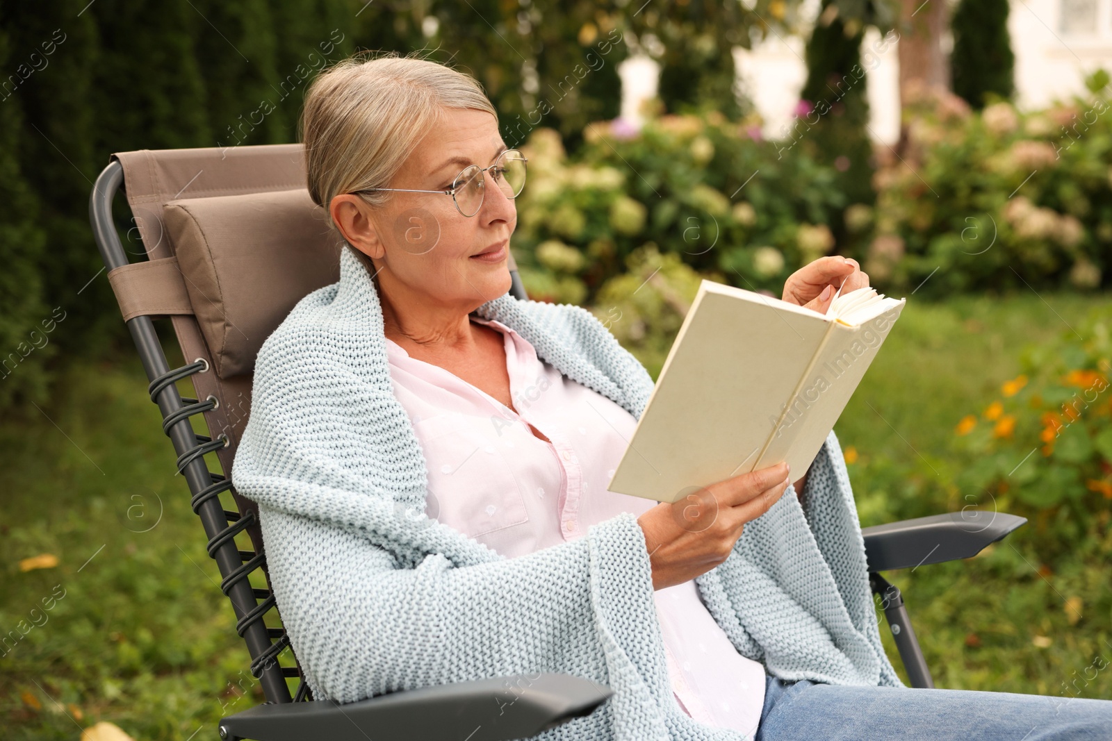 Photo of Senior woman reading book in armchair outdoors