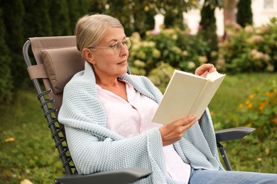 Photo of Senior woman reading book in armchair outdoors