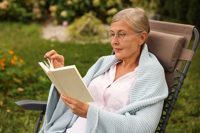Photo of Senior woman reading book in armchair outdoors