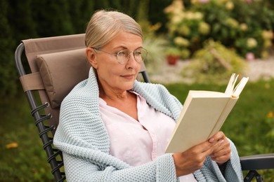 Photo of Senior woman reading book in armchair outdoors