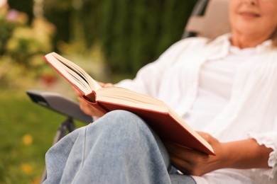 Photo of Senior woman reading book in armchair outdoors, closeup