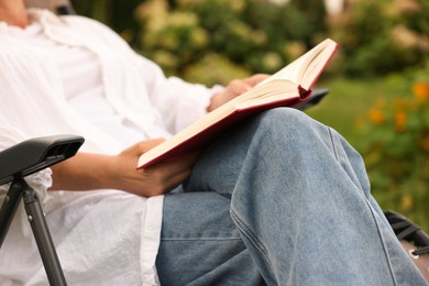 Photo of Senior woman reading book in armchair outdoors, closeup