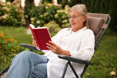 Photo of Senior woman reading book in armchair outdoors